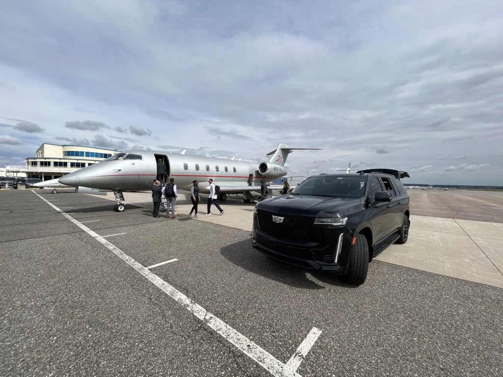 Black Cadillac SUV staged beside a private jet for private aviation transportation